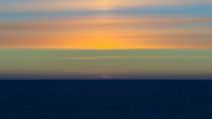 Sun’s green flash visible at sunset, with colorful cloud-filled sky.