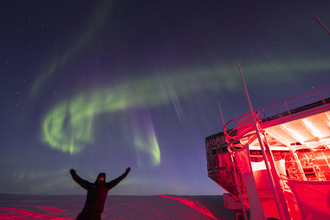 Person with arms thrown up into the air, with swirling aurora just overhead.