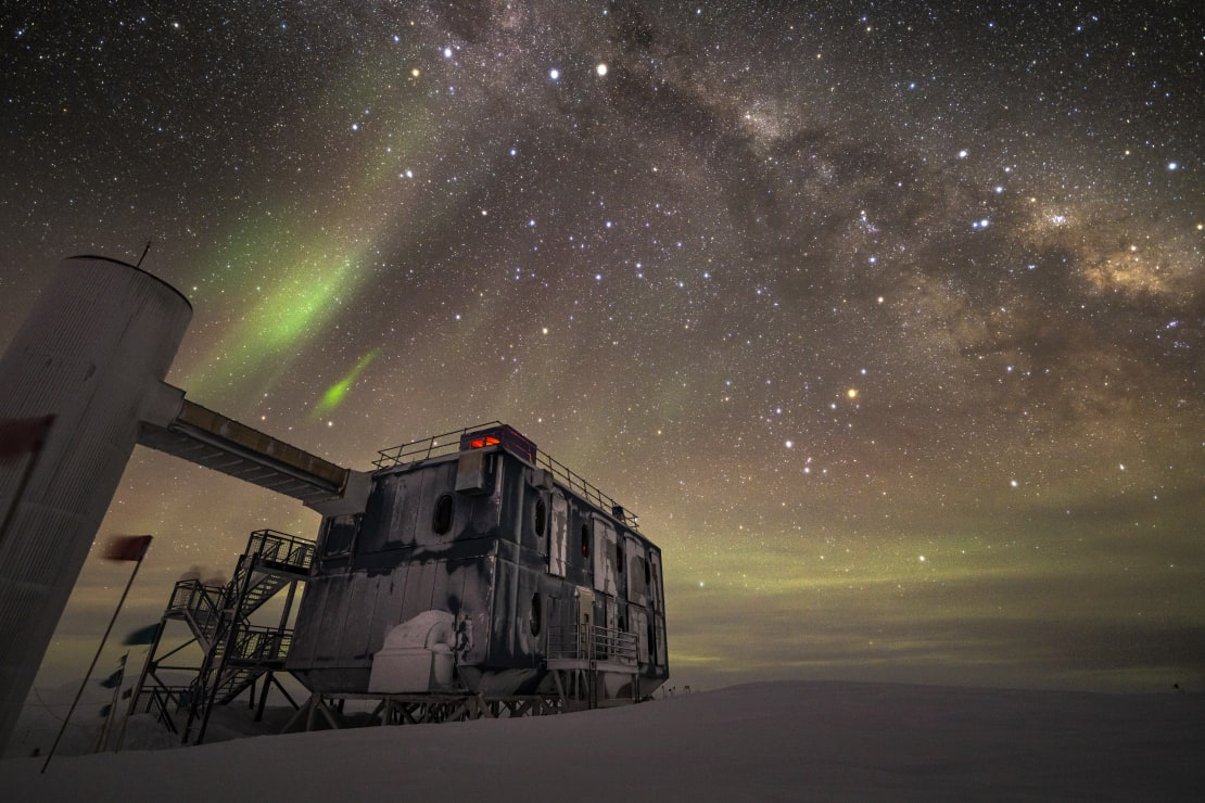 The backside of the IceCube Lab under a starry and aurora-filled sky.