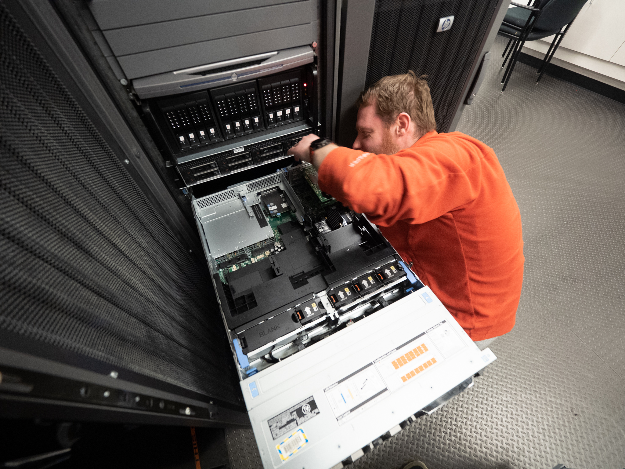 Person crouched over computer rack.