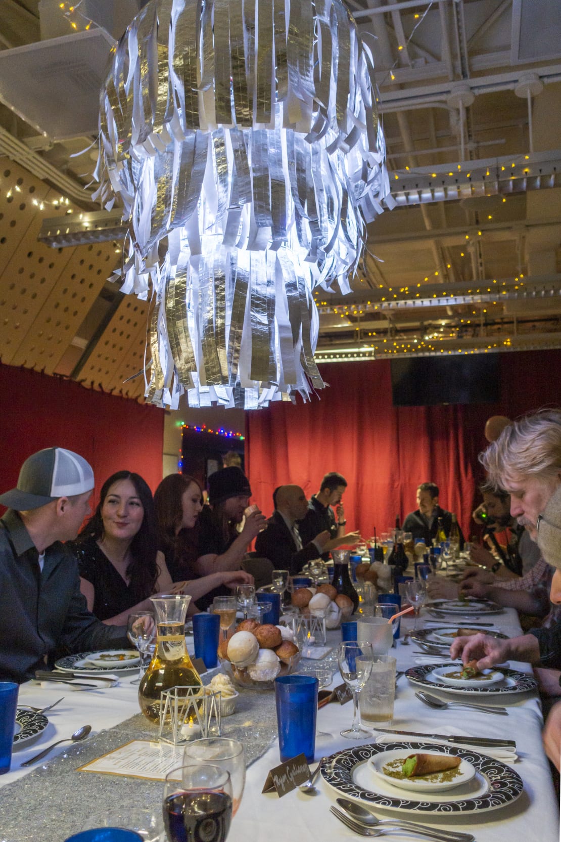 Long view of dinner table, with fancy chandelier overhead in foreground.