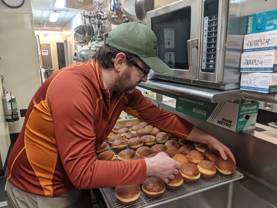 Person arranging donuts on a cooling rack.