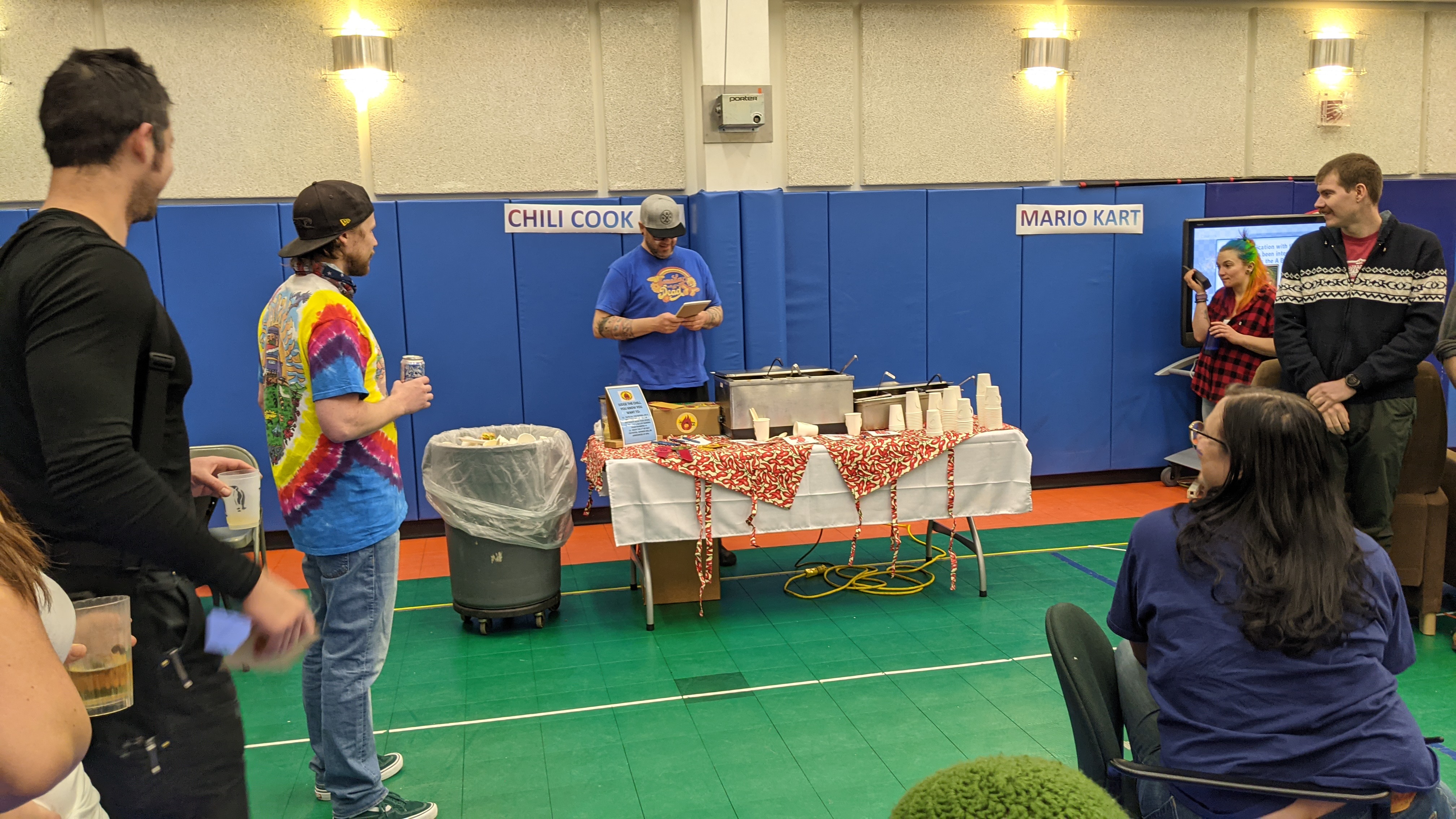 People gathered around chili cookoff table in gym.