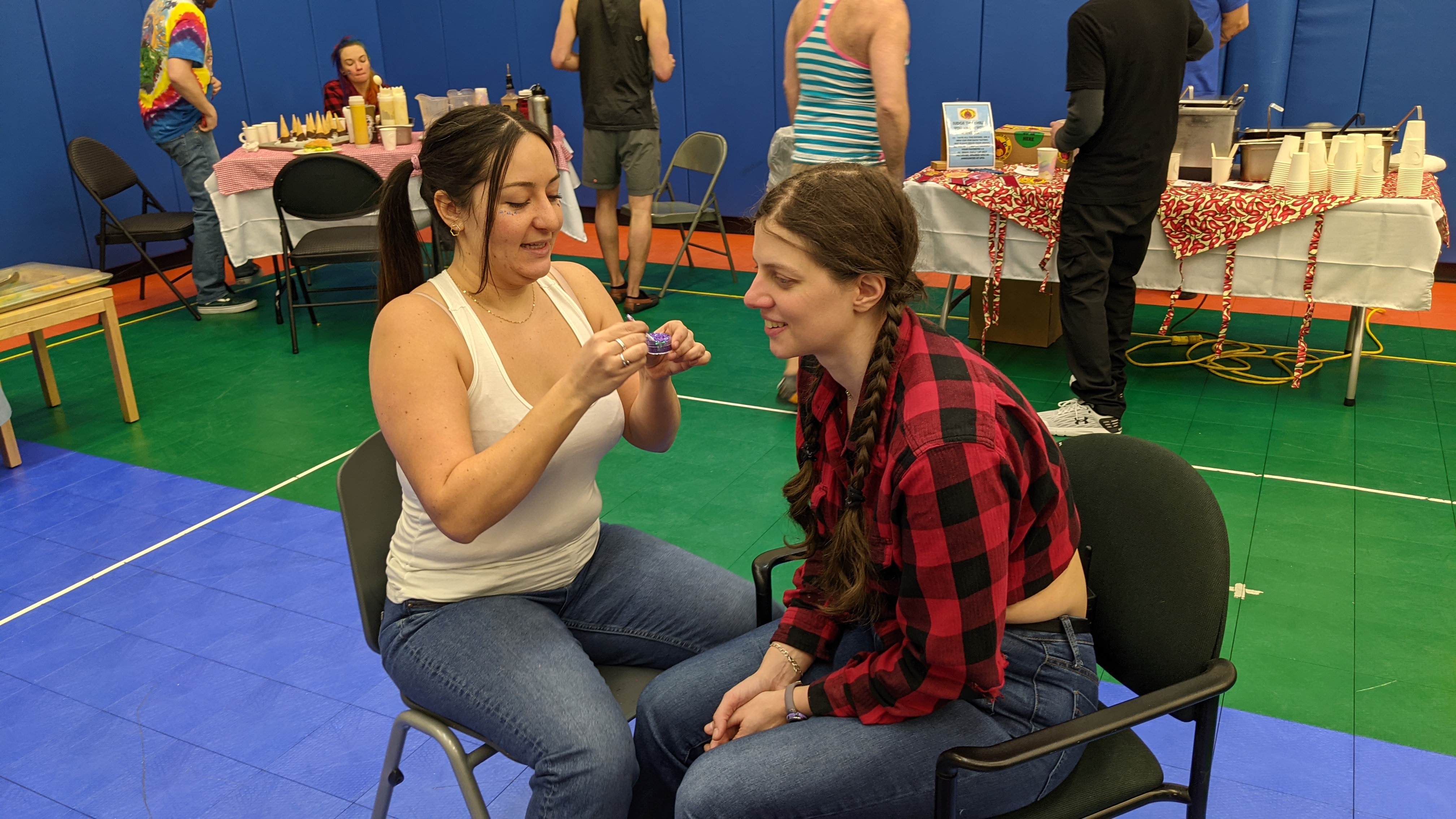 Two people seated in facing chairs for face painting.