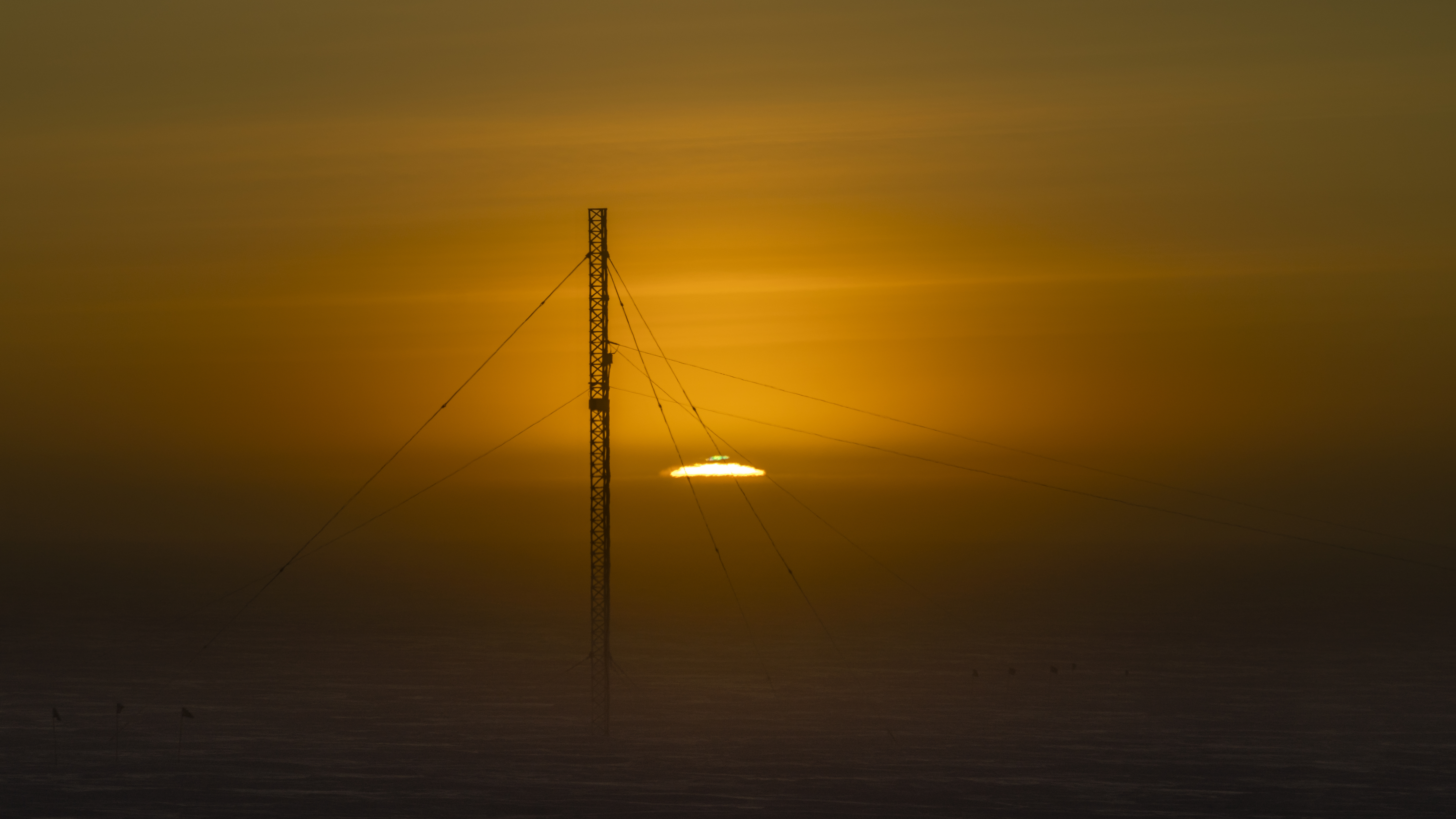 Sun rising at the South Pole, just at horizon with green flash visible, communications tower in foreground.