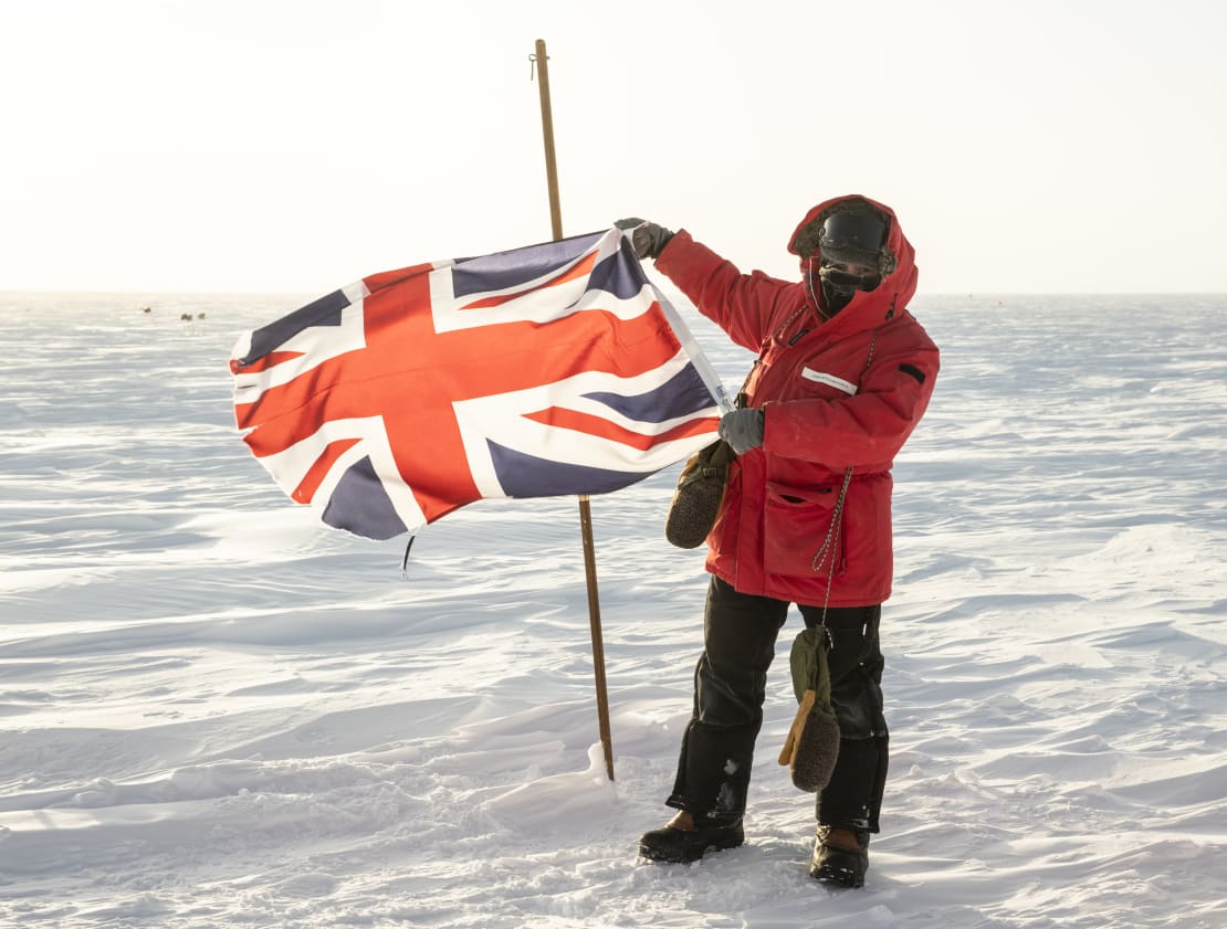 IceCube winterover Josh standing next to British flag.