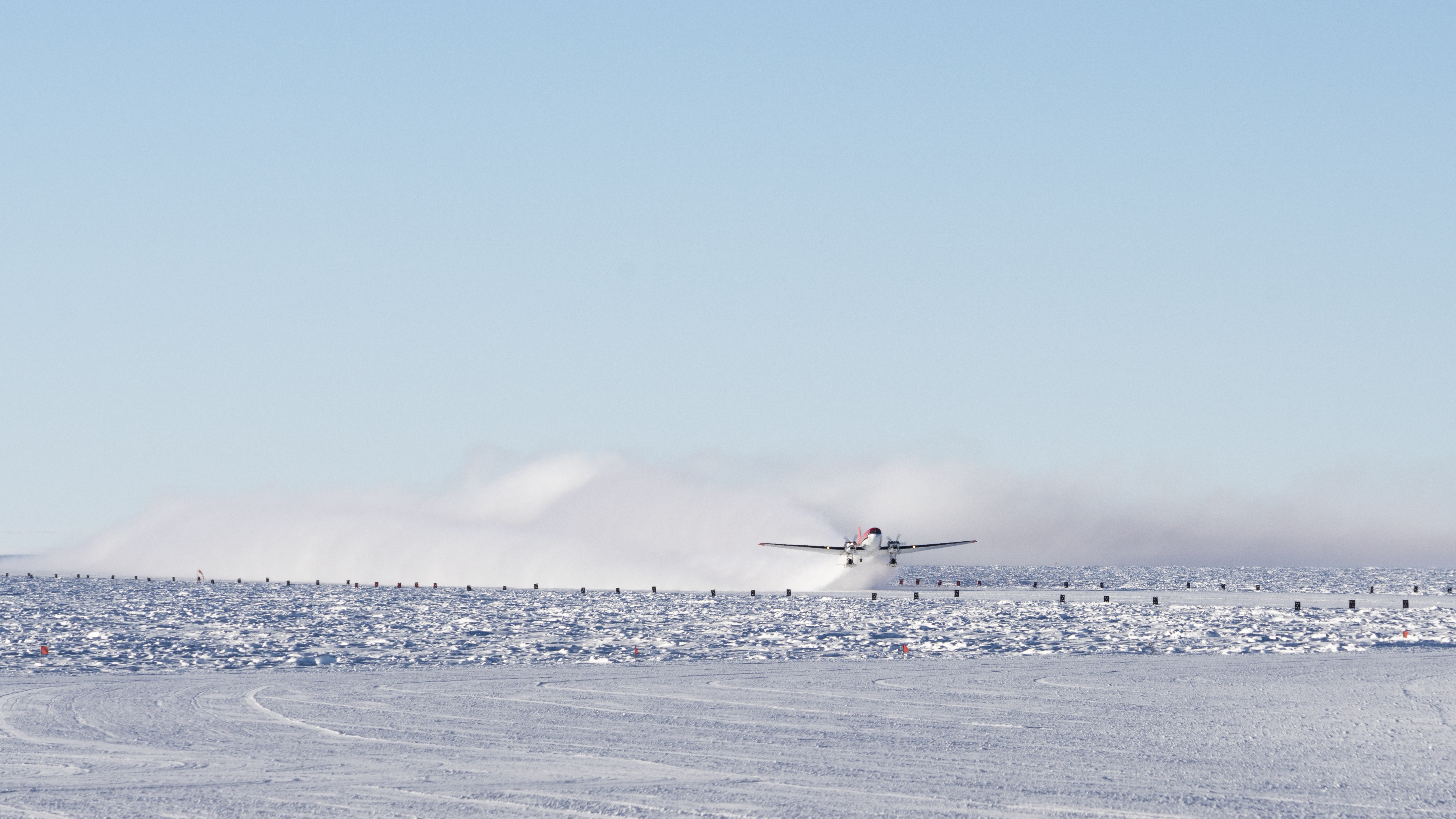 Airplane in distance, taking off from South Pole icy surface.