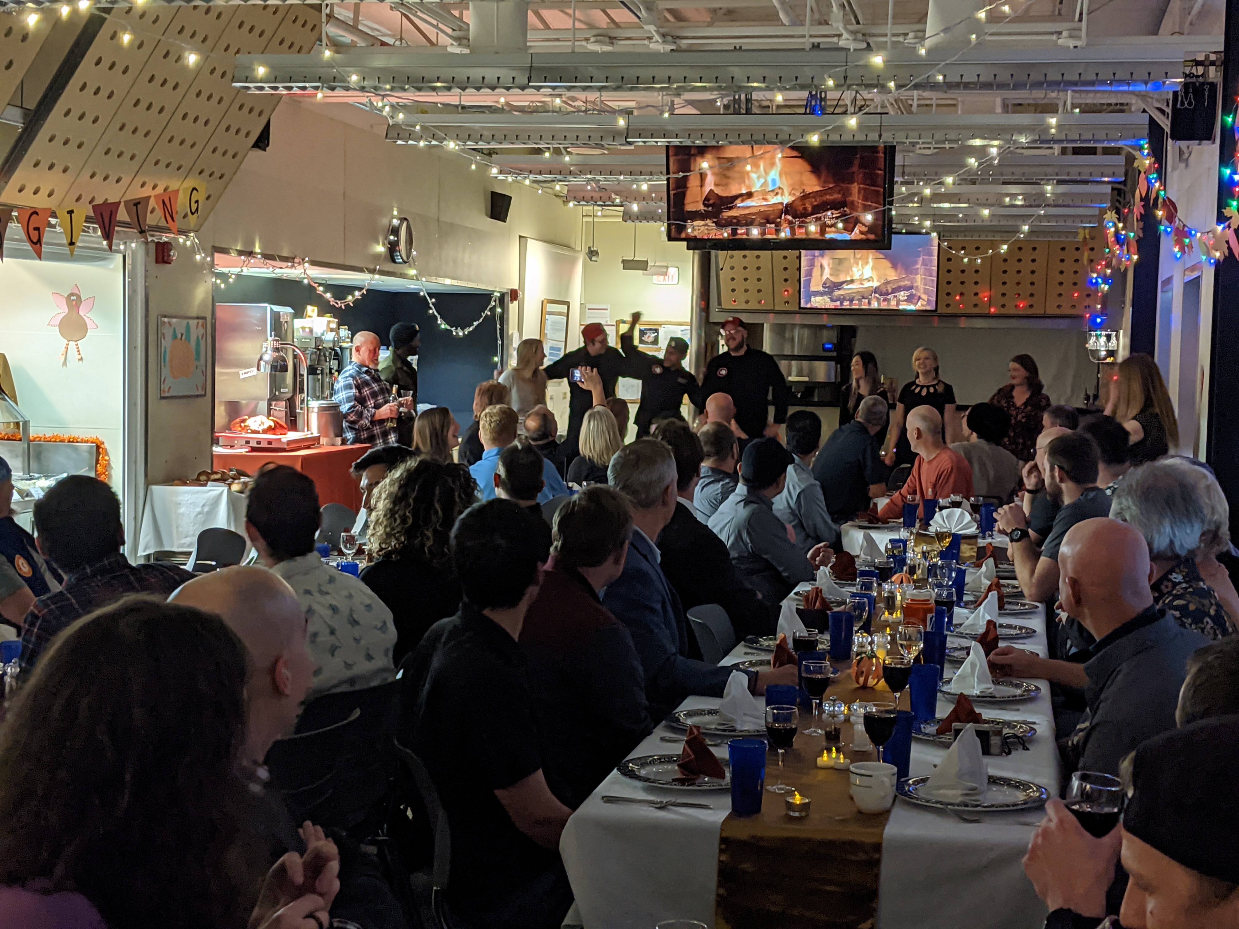 People seated at long tables in the South Pole station galley, looking toward group of individuals standing at far end of room.