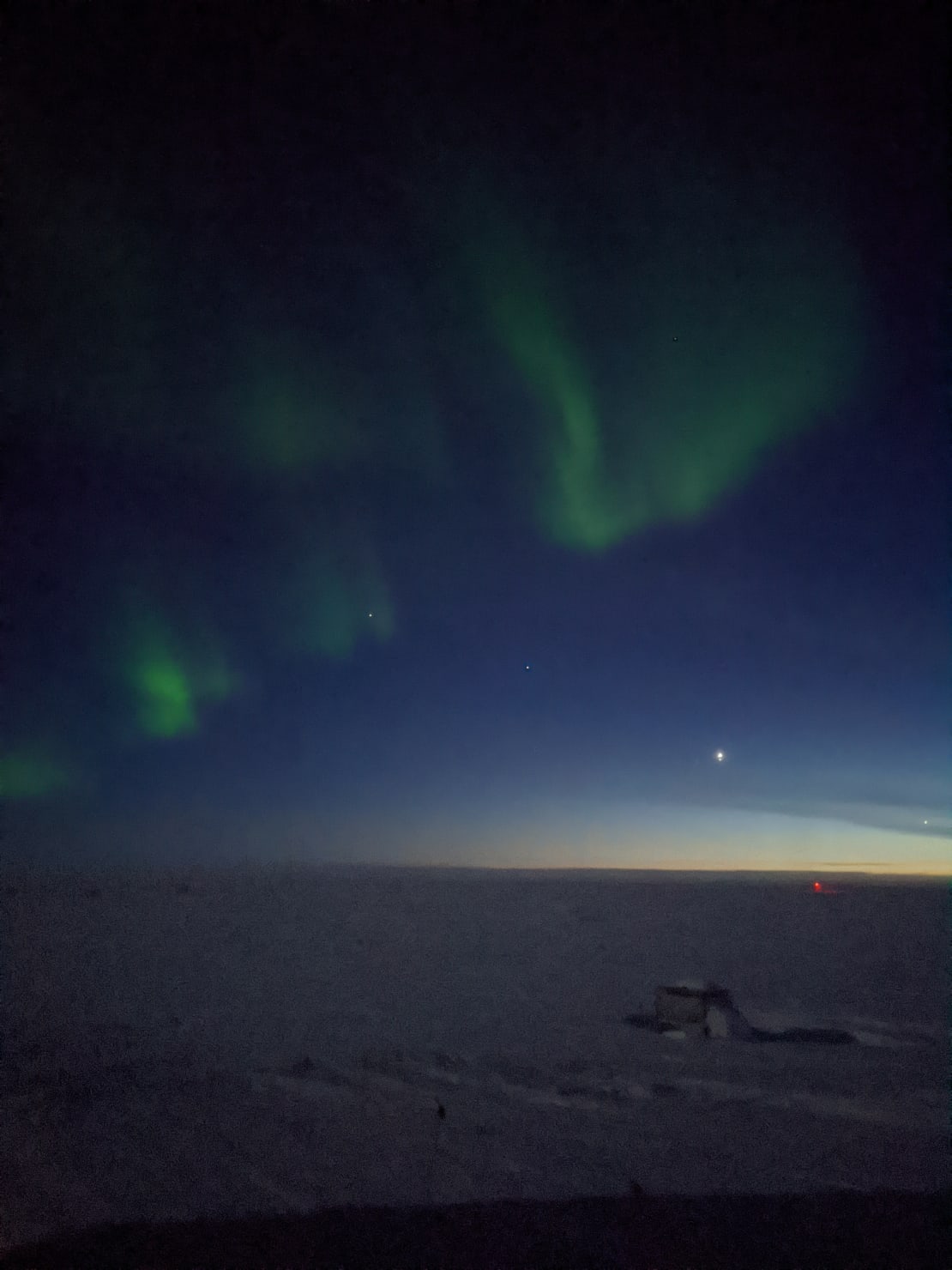 Night sky at the South Pole post sunset, with some light lingering along horizon, a bright planetary conjunction, and light wispy auroras overhead.