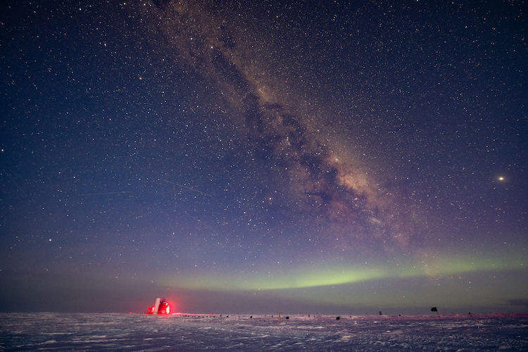 The IceCube Laboratory emitting a red glow against a night sky filled with stars and the Galactic Plange