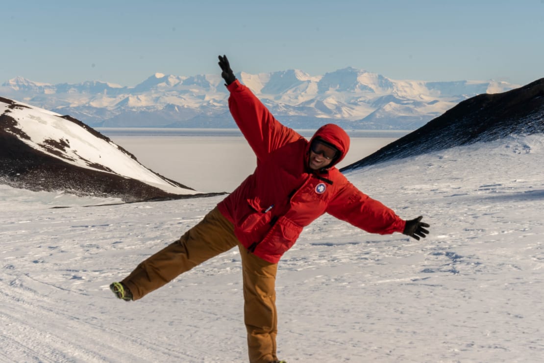 A man in a parka posing with arms and leg up