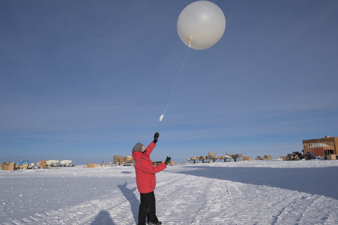 Winterover in red parka out on the ice, just after launching a weather balloon.