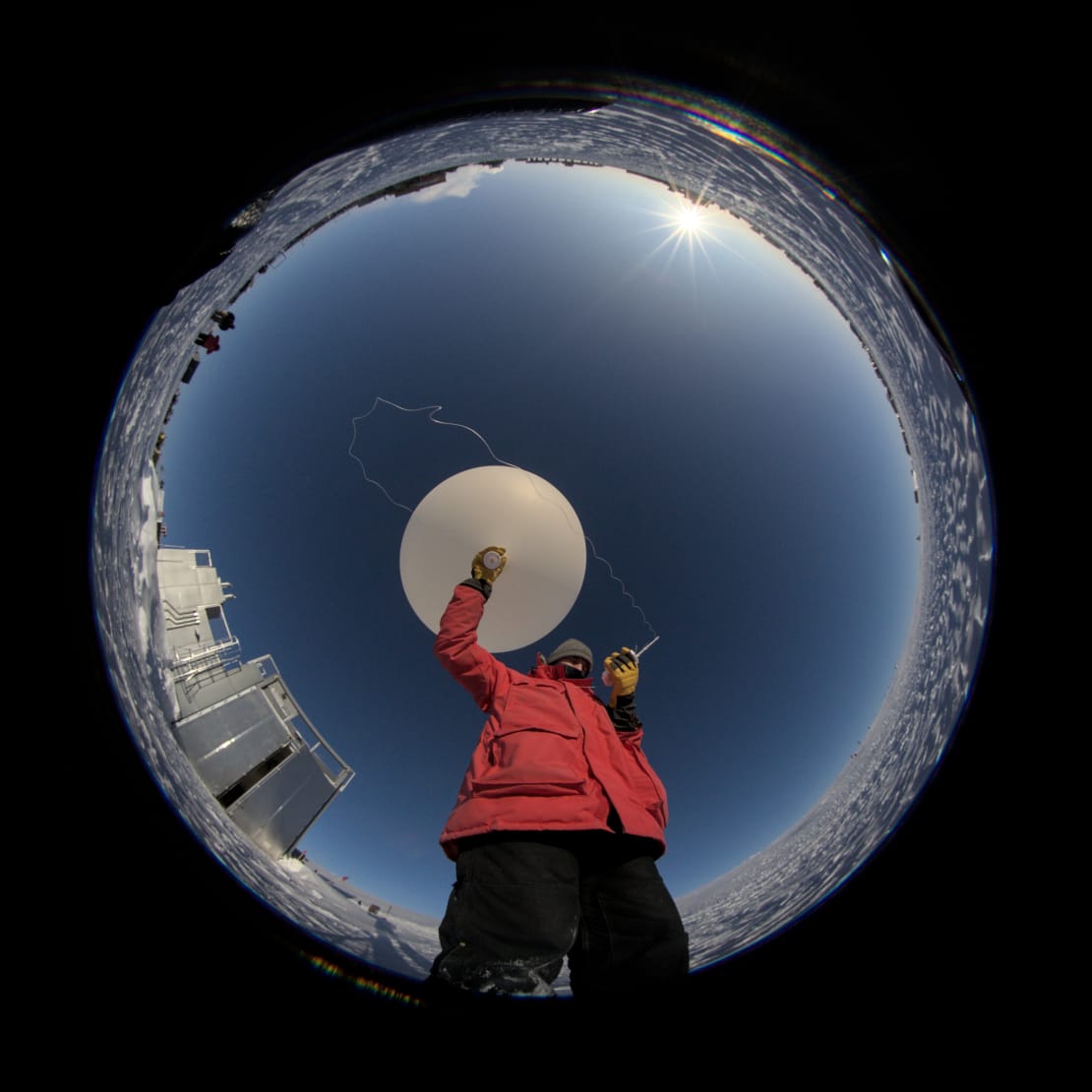 A 360-degree view looking up at winterover holding and ready to launch a weather balloon.