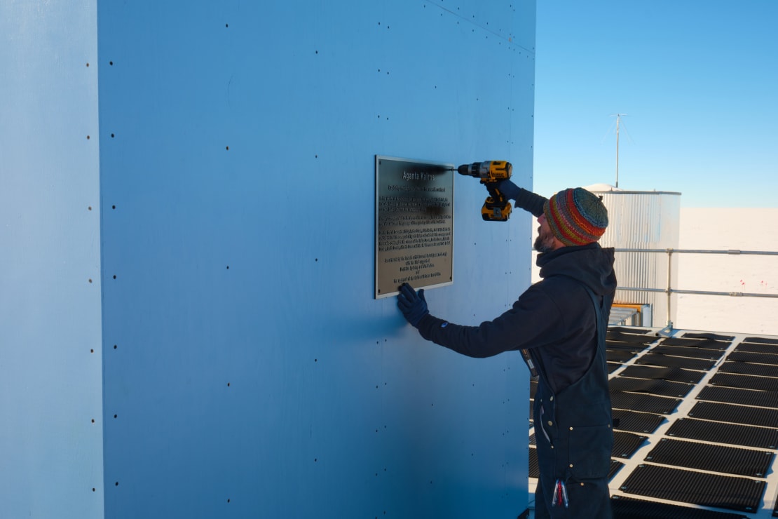 Sideview of person holding up a plaque and fixing its in place against a blue exterior wall.