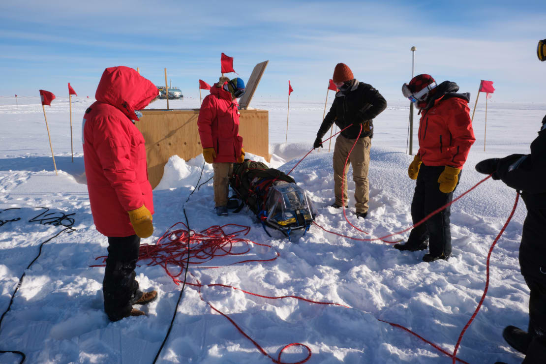 Several people at the Pole working outside on cabling a rigged up sled for a training exercise.