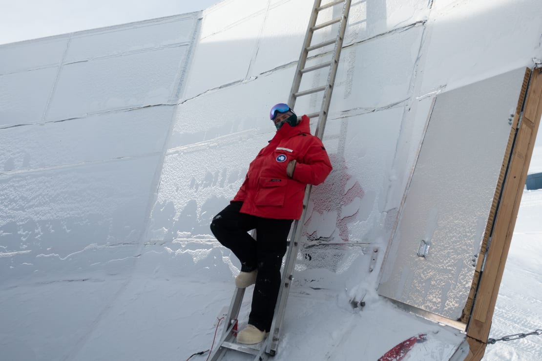 Winterover in red parka leaning back against ladder set up inside BICEP telescope dish at the South Pole.