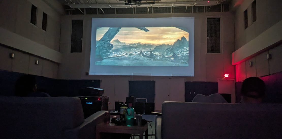 Darkened room with large projection screen showing a movie.