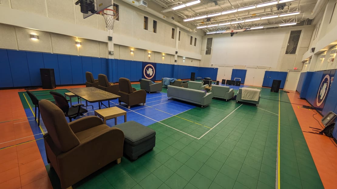 Gymnasium set up with sofas and arm chairs facing a large projection screen on the far wall.