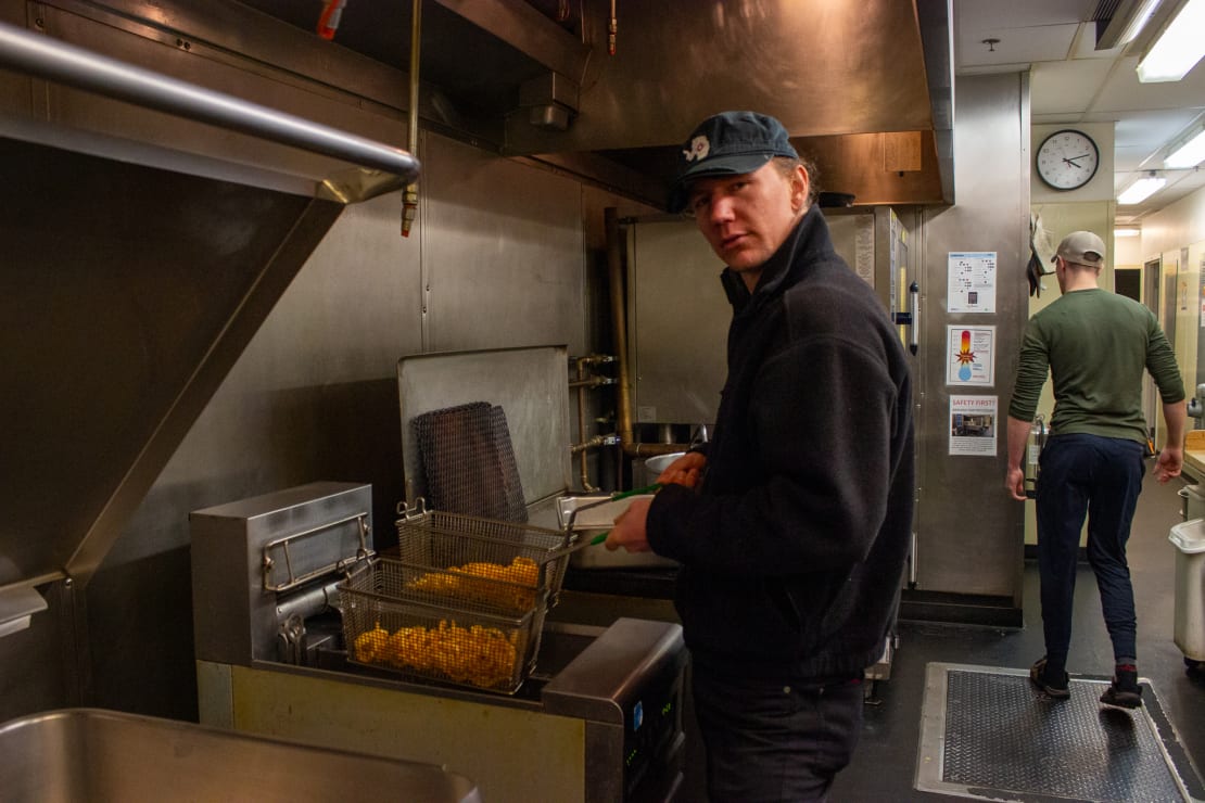 Person facing the camera as they’re pulling up fryer baskets in an industrial kitchen.