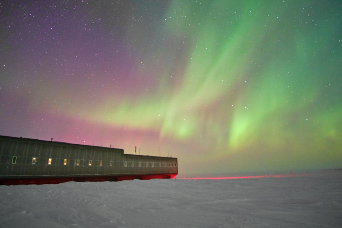 Colorful auroras filling the sky at the South Pole, with the station to the left in the foreground