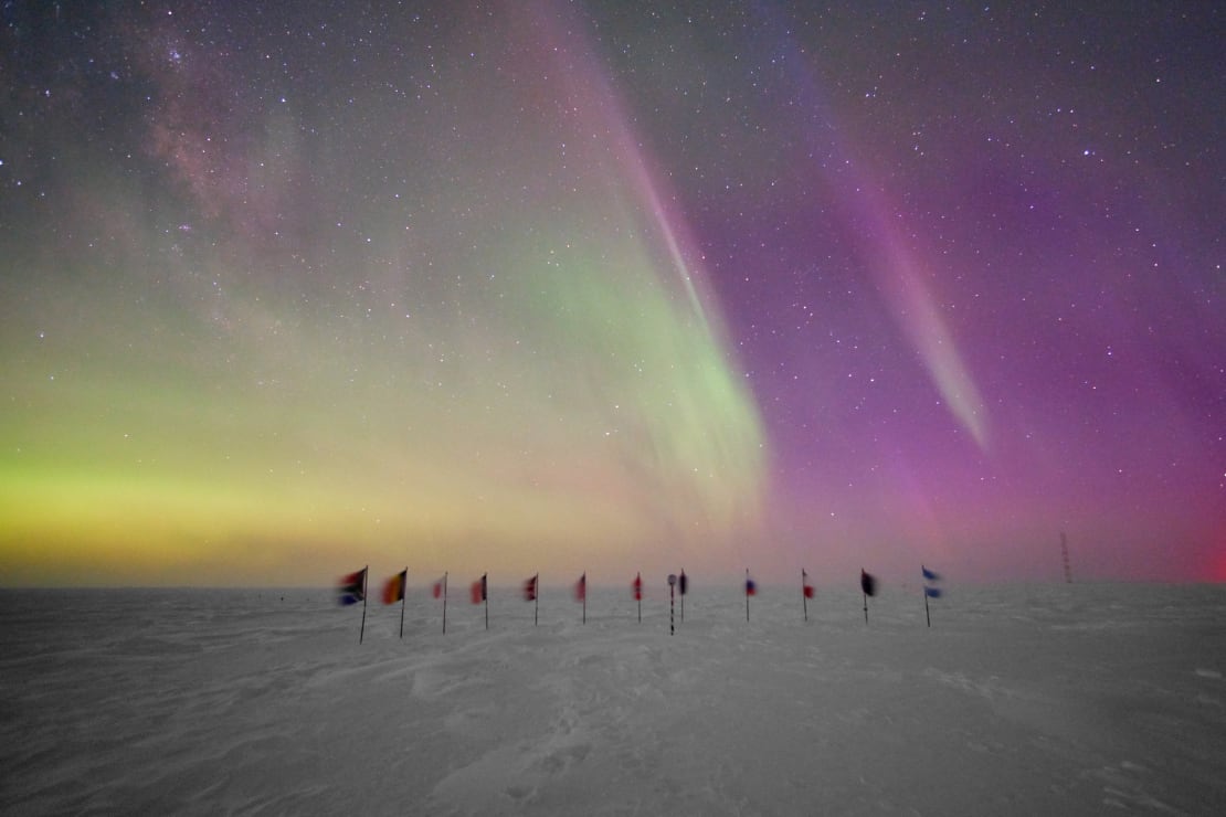 Colorful auroras filling the sky above the flags at the ceremonial Pole.