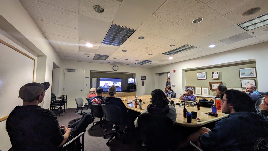 View from back corner of conference room, with group gathered facing a screen at far end.