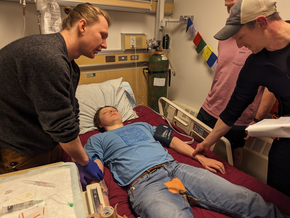 An emergency response exercise showing a patient with eyes closed on their back on a gurney, with several people attending to them.