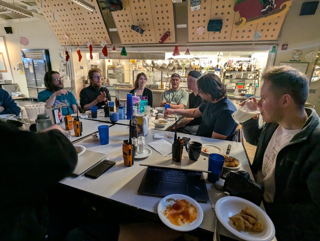 Group seated around a table with food and beverages in the South Pole galley.