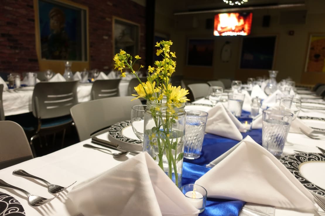 Close-up of flowers in a vase on a long table with formal table settings.