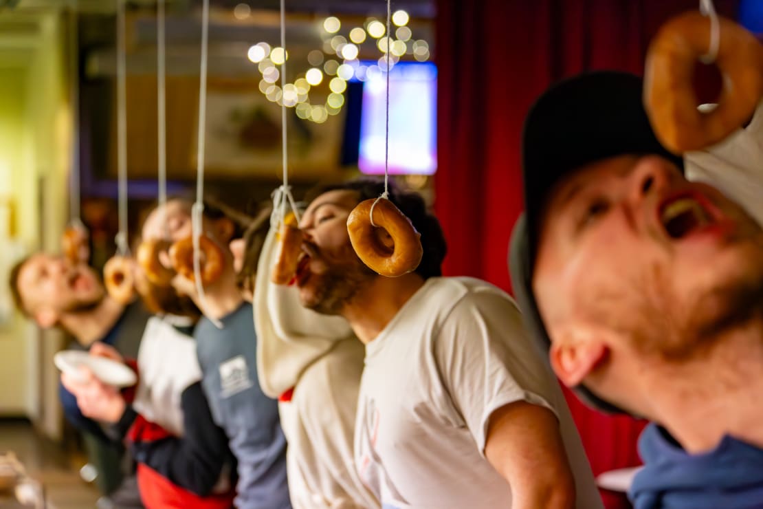 Doughnut eating contest, angled view of doughnuts hanging down from strings and participants trying to eat them from below.