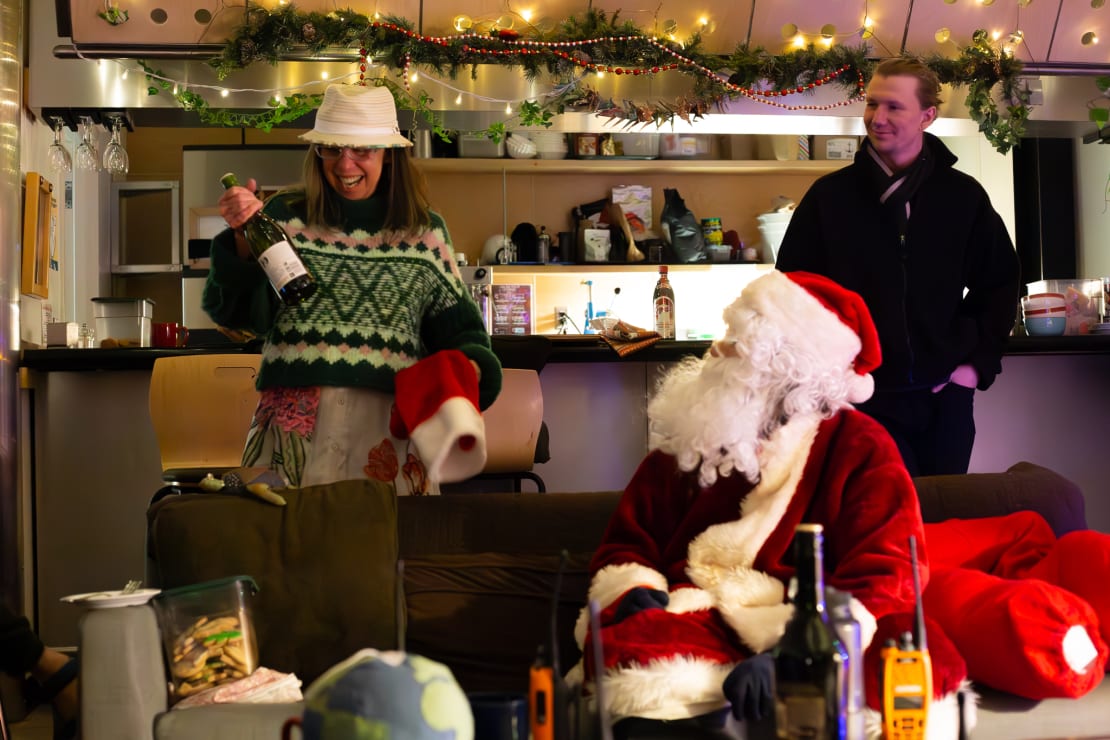 Several people in the middle of opening gifts for Christmas in July, someone in Santa costume seated at table.