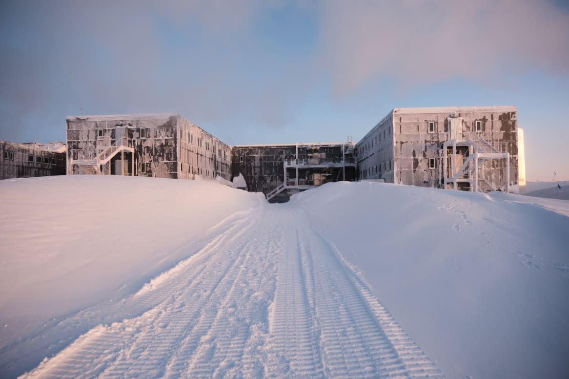 Tall snowdrifts lining a path facing the back of the South Pole station.