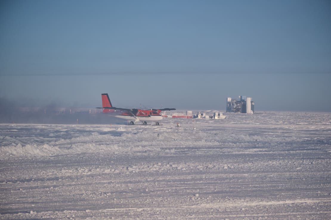 A twin otter landing at the Pole, with the IceCube Lab in background.