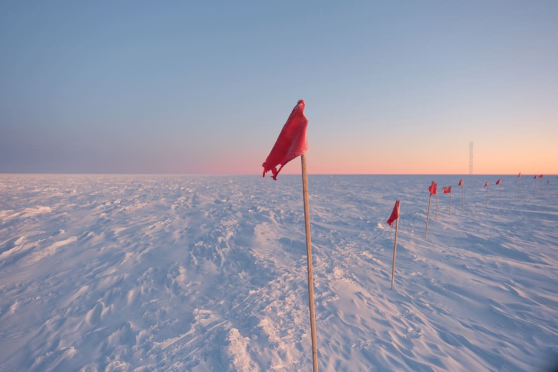 A red flag in foreground and the rest of flag line receding into background at sunrise at the South Pole.