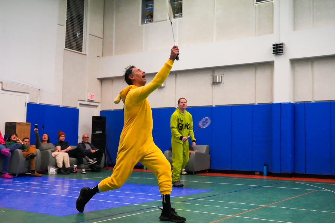 South Pole gym, person in yellow jumpsuit costume in mid-stroke playing badminton.