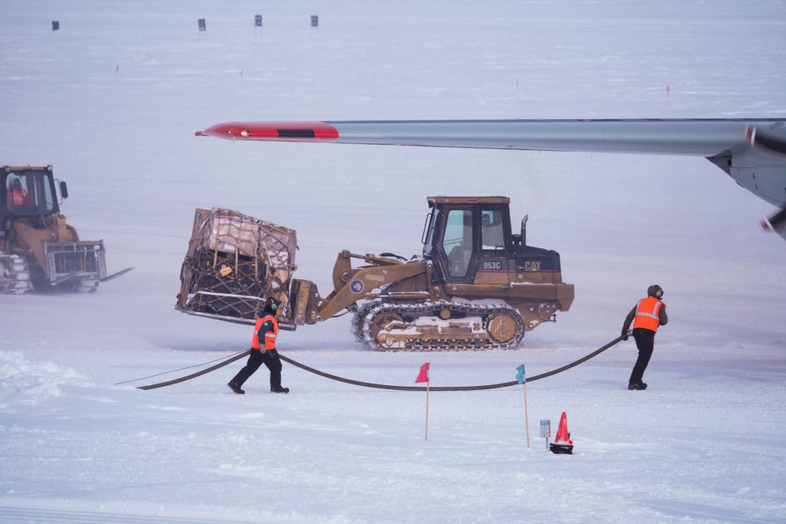 Cargo being taken away from a C-130 LC with fuelies carrying a fuel line.