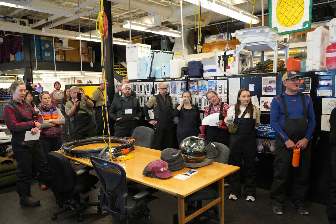 Group of people indoors gathered together listening to someone offscreen.