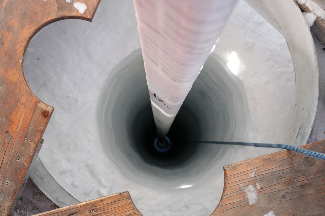 Close-up view down into a deep hole drilled in the ice.