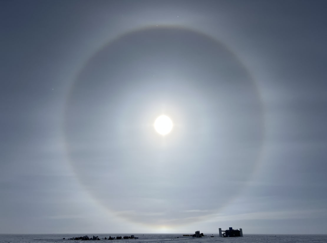 A clear sun halo looming large over the IceCube Lab and equipment site in the distance.