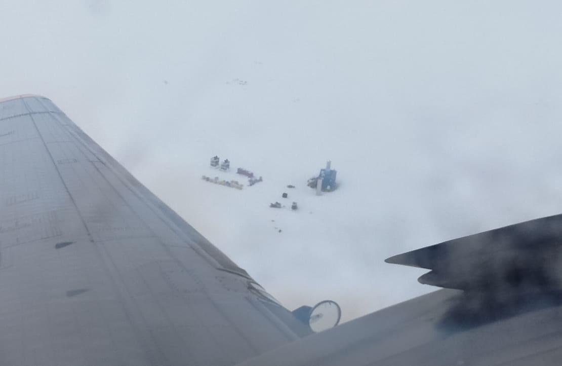 A high-up view of the IceCube Lab and nearby equipment from the window of a departing plane.