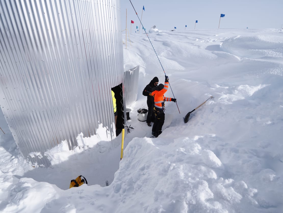 A few people working in a snow trench outside a vertical tower.