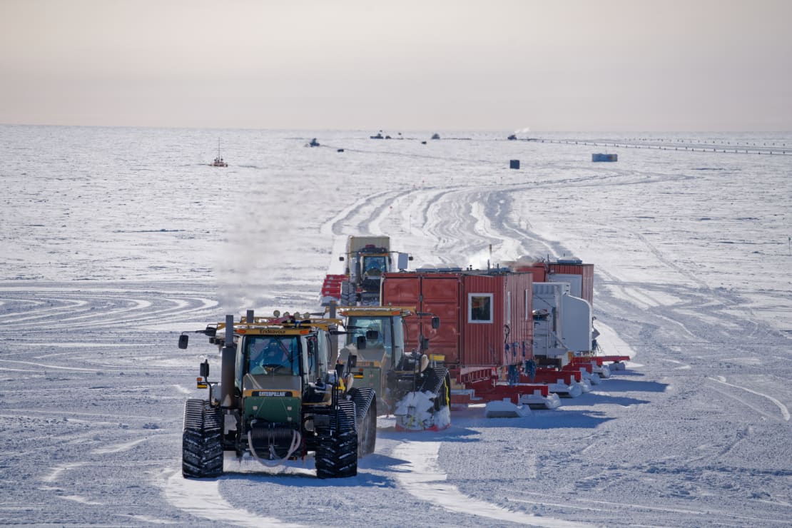 Out on the ice, a group of snow vehicles approaching in the foreground, other groups in the distance.