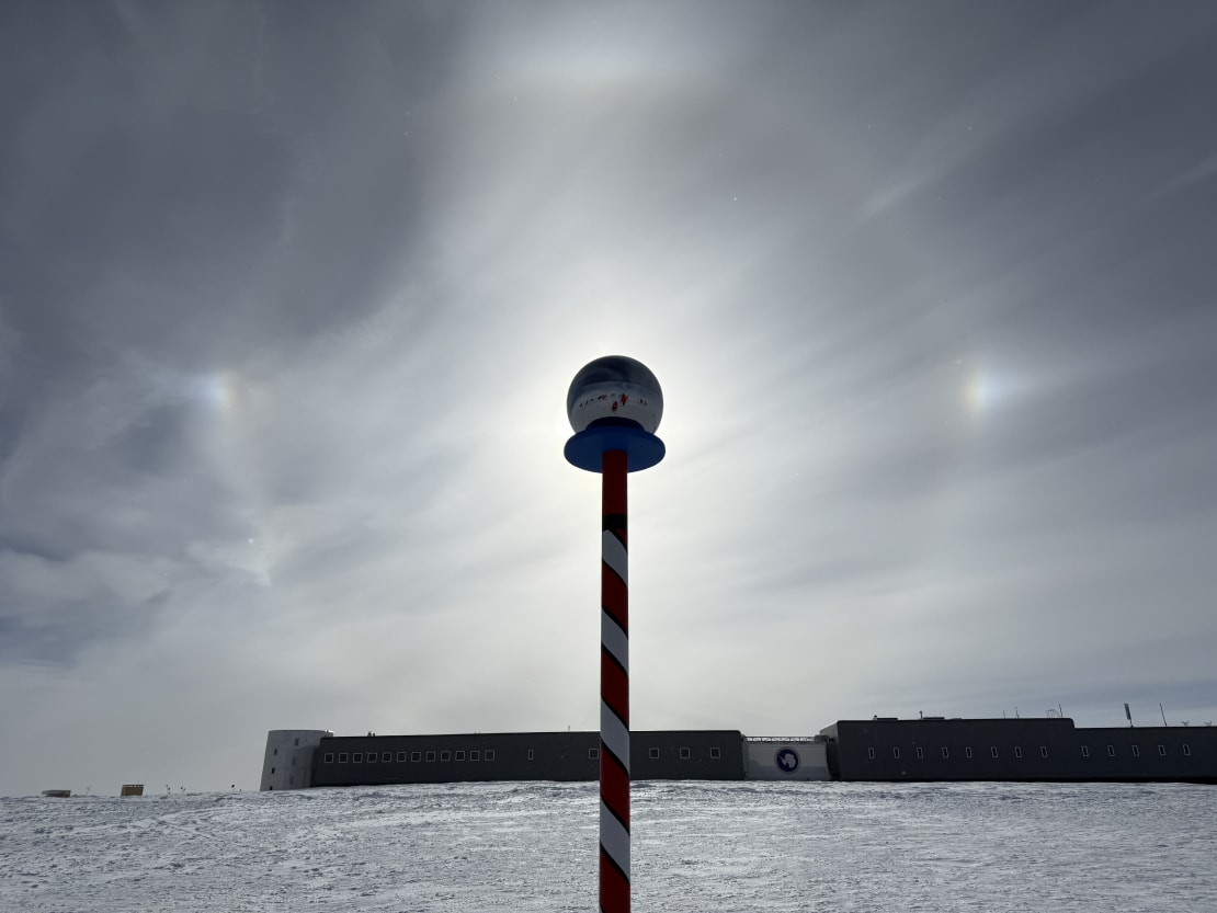 Sun halo and sun dogs, with the sun in the middle blocked by the marker at the ceremonial South Pole.