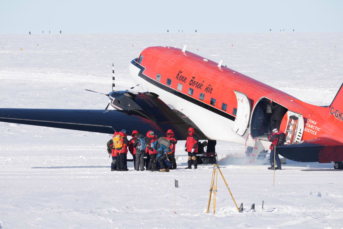 Small group of people on the ice just outside a parked Basler plane.