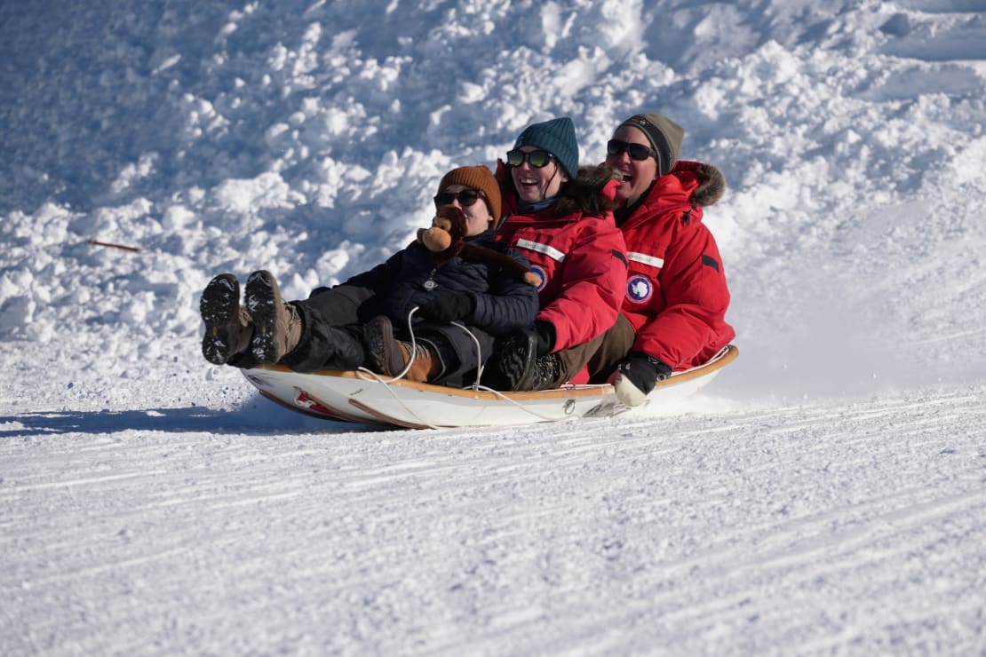 Three people on a sled, smiling, as they reach the bottom of the hill.