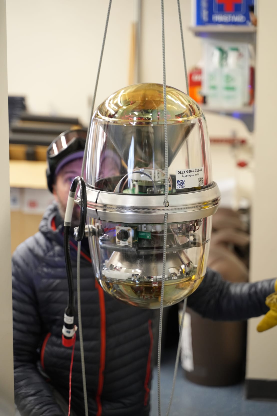 Close-up of new optical module suspended on cables, with person out of focus facing the module.