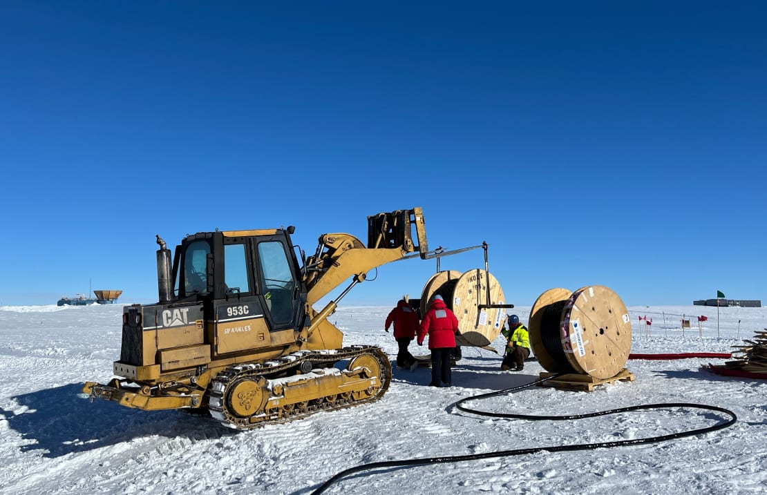 Heavy machinery and a few workers out on ice under clear skies.