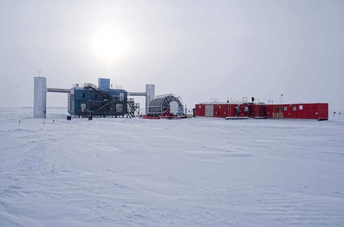 View of IceCube Lab on the right under overcast sky, with nearby hose reel and containers on the left.