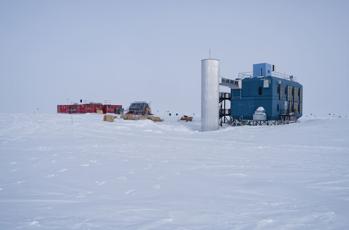 View of IceCube Lab on the right under overcast sky, with nearby hose reel and containers on the left.