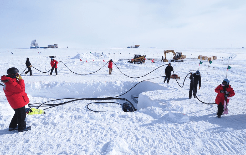 A group of people help thread the cable through the snow at the South Pole